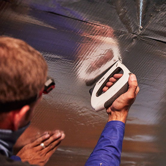 Closeup-of-a-HeatBusters-technician-using-a-tool-to-install-radiant-barrier-insulation-2