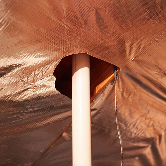 A piece of the radiant barrier is removed to allow space for a vertical standing pipe.