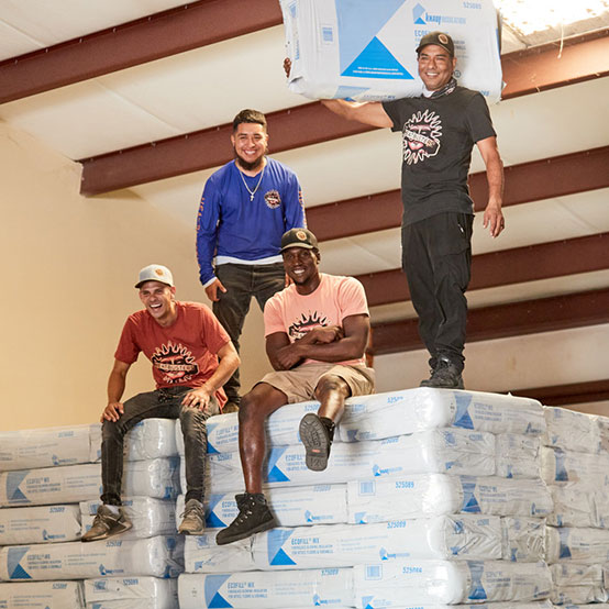 The HeatBusters team sit on stacks of Ecofill insulation laughing.